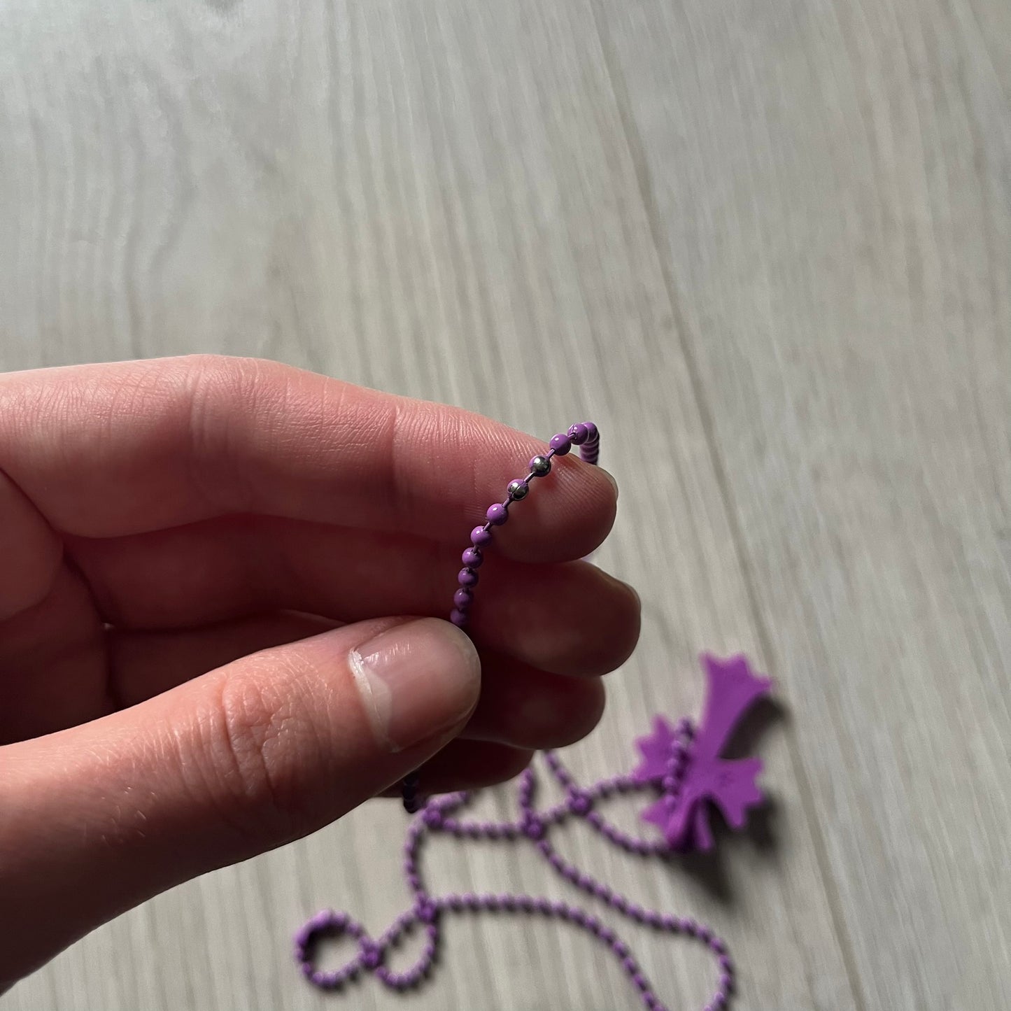 The Chrome Hearts 'Silichrome' Cross Purple Necklace showcases a silicone cross pendant with embossed CH lettering, twin cross graphics on the back, and a 2019 anniversary mark. Offered only through CH flagship stores, it comes paired with a purple ball chain and includes both the dustbag and paper receipt.