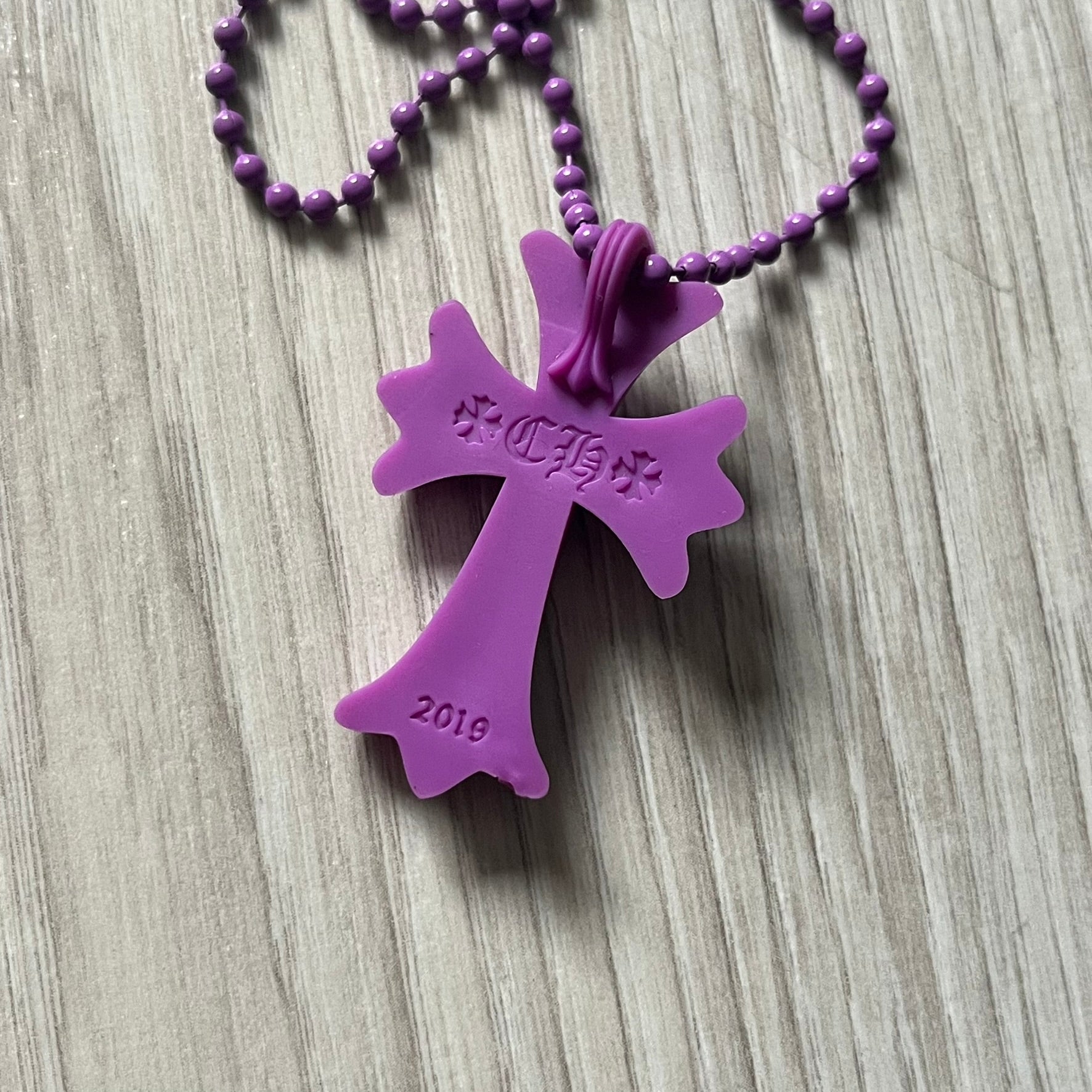 The Chrome Hearts 'Silichrome' Cross Purple Necklace showcases a silicone cross pendant with embossed CH lettering, twin cross graphics on the back, and a 2019 anniversary mark. Offered only through CH flagship stores, it comes paired with a purple ball chain and includes both the dustbag and paper receipt.