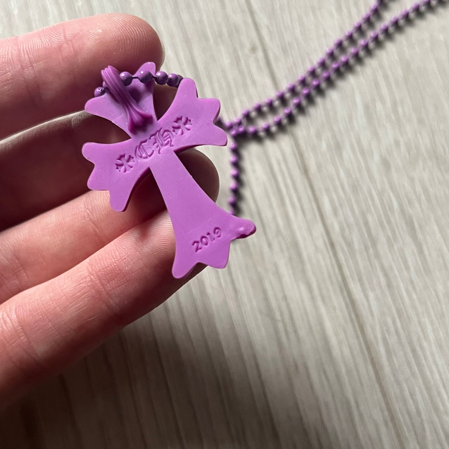 The Chrome Hearts 'Silichrome' Cross Purple Necklace showcases a silicone cross pendant with embossed CH lettering, twin cross graphics on the back, and a 2019 anniversary mark. Offered only through CH flagship stores, it comes paired with a purple ball chain and includes both the dustbag and paper receipt.