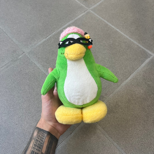 Club Penguin 2009 Series 3 Aunt Arctic Penguin Plushie is a green penguin with a pink beanie, freckles, black eyeglasses and a pencil next to the ear. Released in [year] by Disney and Jakks Pacific, featuring an embroidered Club Penguin logo on the bottom of the foot. It comes with a Disney-licensed tag.