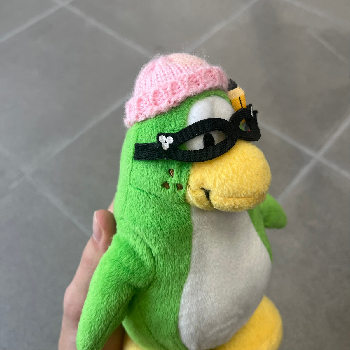 Club Penguin 2009 Series 3 Aunt Arctic Penguin Plushie is a green penguin with a pink beanie, freckles, black eyeglasses and a pencil next to the ear. Released in [year] by Disney and Jakks Pacific, featuring an embroidered Club Penguin logo on the bottom of the foot. It comes with a Disney-licensed tag.