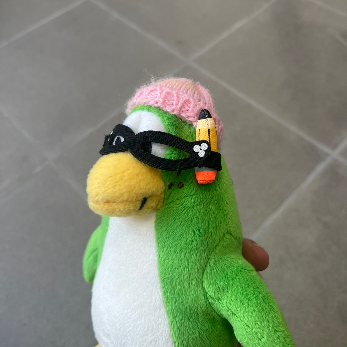 Club Penguin 2009 Series 3 Aunt Arctic Penguin Plushie is a green penguin with a pink beanie, freckles, black eyeglasses and a pencil next to the ear. Released in [year] by Disney and Jakks Pacific, featuring an embroidered Club Penguin logo on the bottom of the foot. It comes with a Disney-licensed tag.