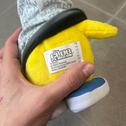 Club Penguin 2010 Series 7 Band Member Penguin Plushie is a yellow penguin with 3D Headphones and a jacket that can be taken off. Released in 2010 by Disney and Jakks Pacific, featuring an embroidered Club Penguin logo on the bottom of the foot. It comes with a Disney-licensed tag.