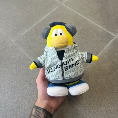 Club Penguin 2010 Series 7 Band Member Penguin Plushie is a yellow penguin with 3D Headphones and a jacket that can be taken off. Released in 2010 by Disney and Jakks Pacific, featuring an embroidered Club Penguin logo on the bottom of the foot. It comes with a Disney-licensed tag.