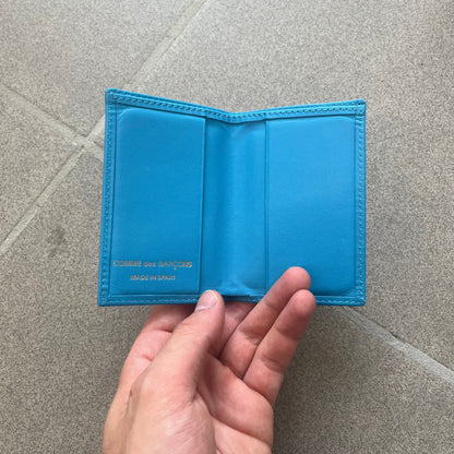 Comme des Garçons Blue Bifold Leather Wallet features a clean and minimal bi-fold design crafted from smooth aqua blue calf leather. The interior includes multiple card slots, a banknote compartment, and a gold-tone Comme des Garçons logo stamp for a subtle branded detail. A timeless everyday accessory combining practical organization with the brand’s signature minimalist aesthetic.
