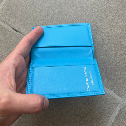 Comme des Garçons Blue Bifold Leather Wallet features a clean and minimal bi-fold design crafted from smooth aqua blue calf leather. The interior includes multiple card slots, a banknote compartment, and a gold-tone Comme des Garçons logo stamp for a subtle branded detail. A timeless everyday accessory combining practical organization with the brand’s signature minimalist aesthetic.
