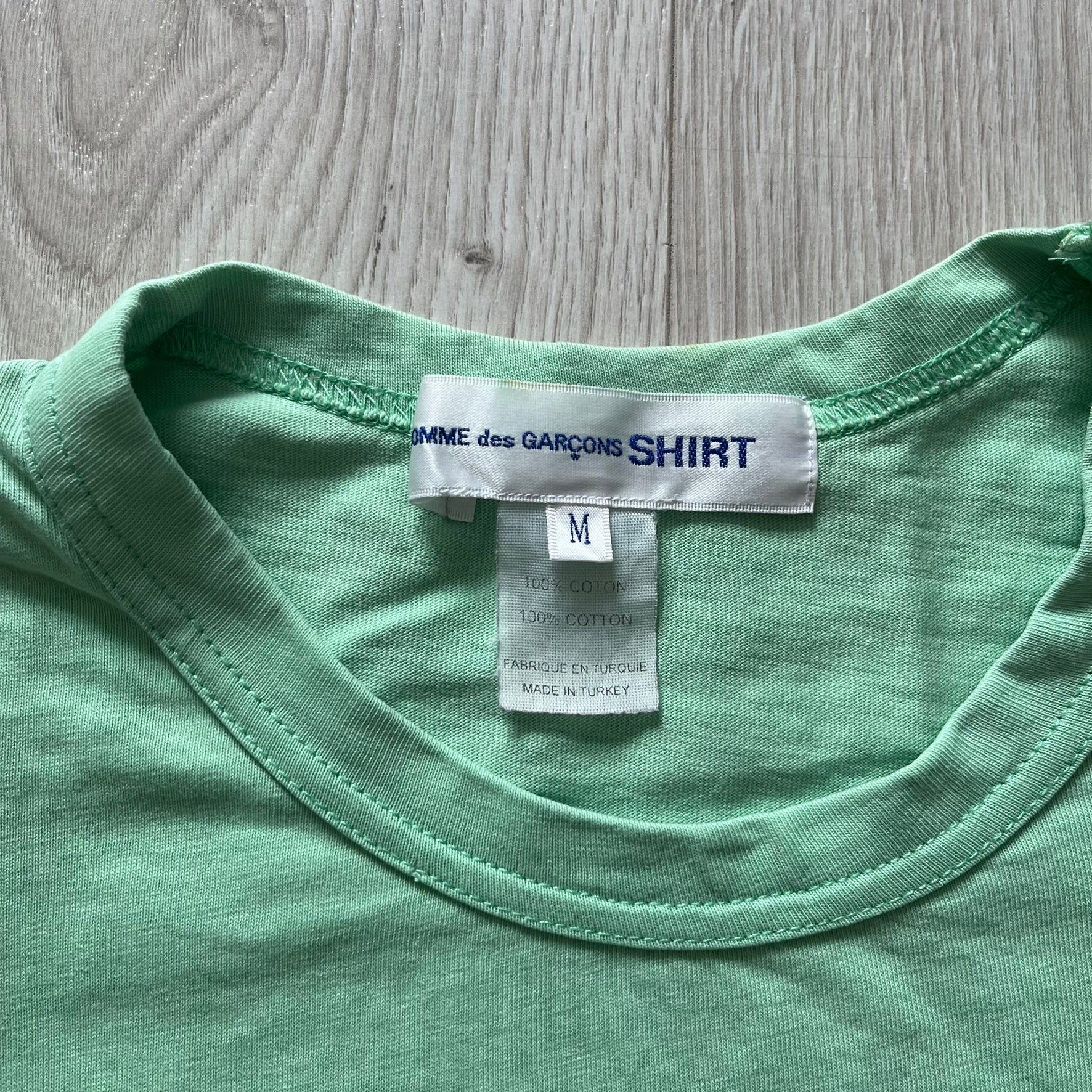 Close-up of a green shirt with a label on a wooden surface