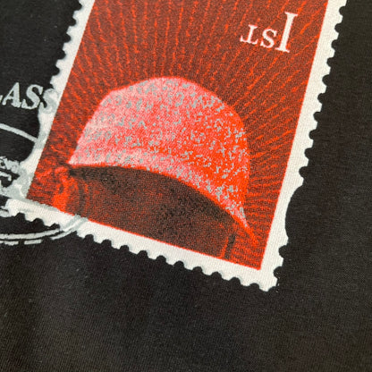 Corteiz x Skepta Konnichiwa 10th Anniversary BlackTee is a 100% cotton T-shirt released to mark the 10th anniversary of Skepta's "Konnichiwa" album, featuring the original album cover artwork with a red postage stamp graphic of Skepta. The design includes a "First Class" ink stamp alongside the Corteiz logo replacing the original cover's "London" mark.