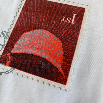 Corteiz x Skepta Konnichiwa 10th Anniversary White Tee is a 100% cotton T-shirt released to mark the 10th anniversary of Skepta's "Konnichiwa" album, featuring the original album cover artwork with a red postage stamp graphic of Skepta. The design includes a "First Class" ink stamp alongside the Corteiz logo replacing the original cover's "London" mark.