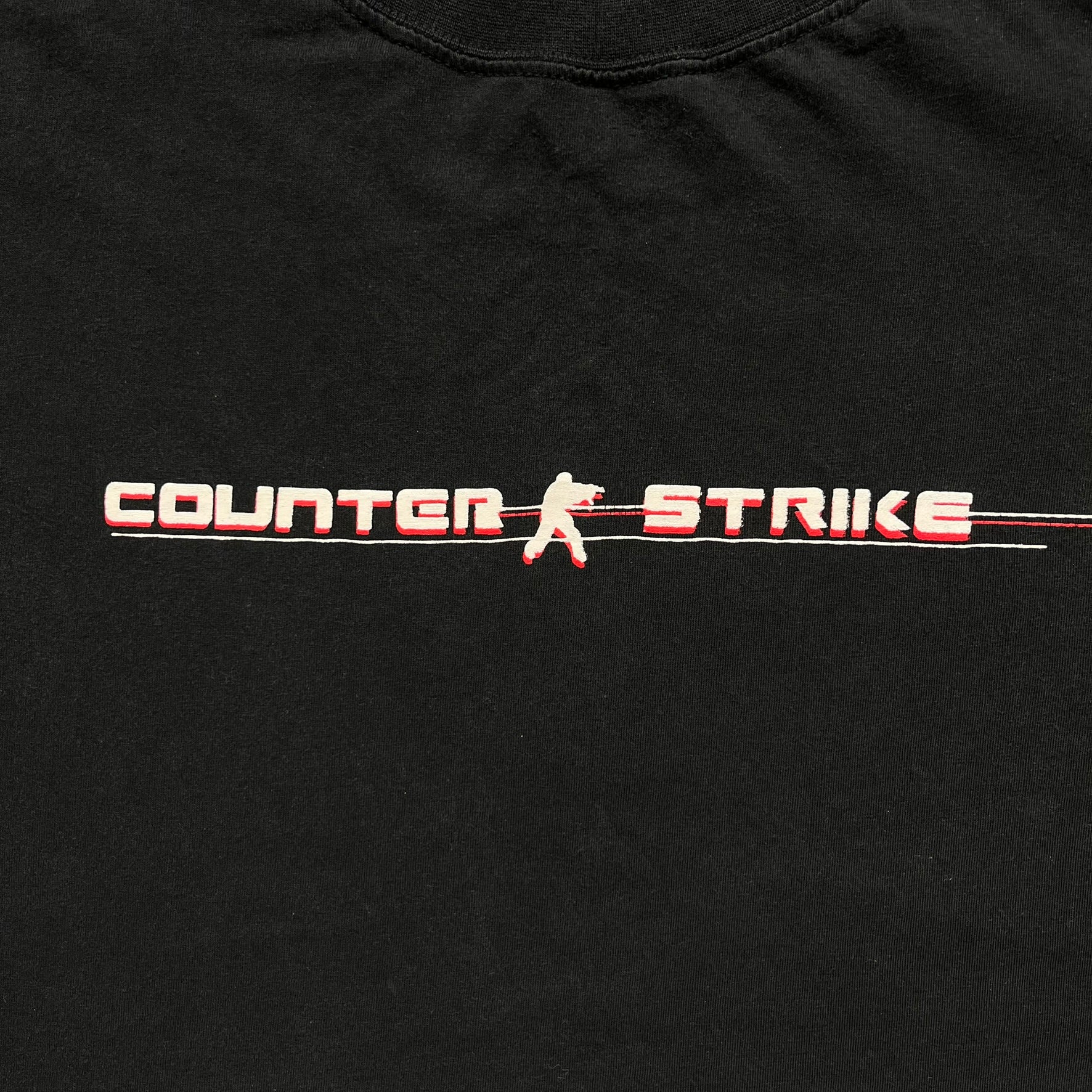 Counter-Strike 2000s Logo Tee is a black T-shirt featuring the classic Counter-Strike logo printed across the front. The design includes white “Counter” and “Strike” text separated by the armed character silhouette, with a red shadow layer behind the logo. A small red Ben Hao tag is attached near the bottom hem.