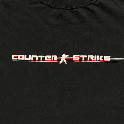 Counter-Strike 2000s Logo Tee is a black T-shirt featuring the classic Counter-Strike logo printed across the front. The design includes white “Counter” and “Strike” text separated by the armed character silhouette, with a red shadow layer behind the logo. A small red Ben Hao tag is attached near the bottom hem.