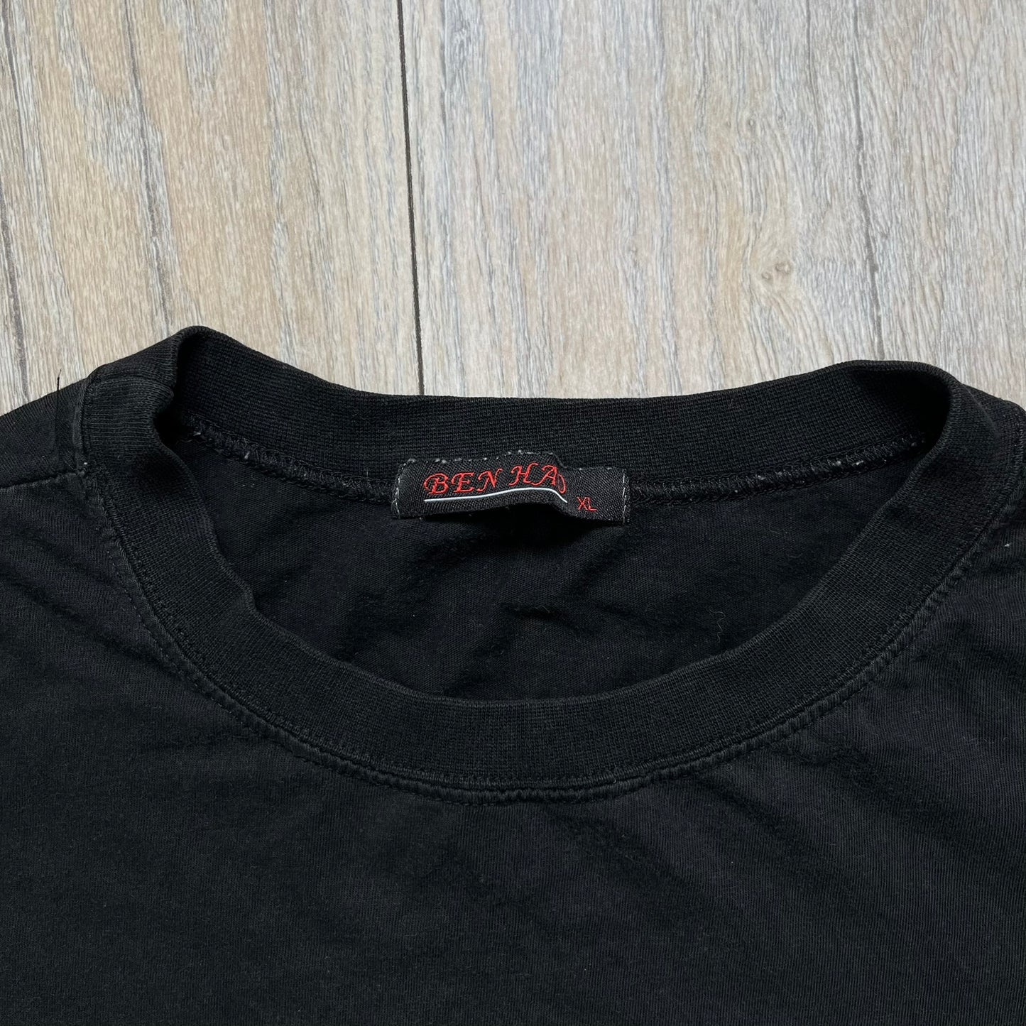 Counter-Strike 2000s Logo Tee is a black T-shirt featuring the classic Counter-Strike logo printed across the front. The design includes white “Counter” and “Strike” text separated by the armed character silhouette, with a red shadow layer behind the logo. A small red Ben Hao tag is attached near the bottom hem.