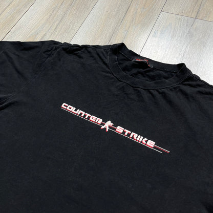 Counter-Strike 2000s Logo Tee is a black T-shirt featuring the classic Counter-Strike logo printed across the front. The design includes white “Counter” and “Strike” text separated by the armed character silhouette, with a red shadow layer behind the logo. A small red Ben Hao tag is attached near the bottom hem.