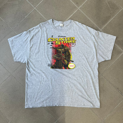 Counter Strike 2015 Arcade Block Gray Tee is a gray T-shirt featuring two Counter-Terrorists in yellow tones on a red background, with a yellow Counter-Strike text logo and a Nokami logo above the graphic. Two “Notindendo” logos sit on either side of the artwork. The shirt was available in the 2015 Arcade Block, specifically in the Nerd Block.