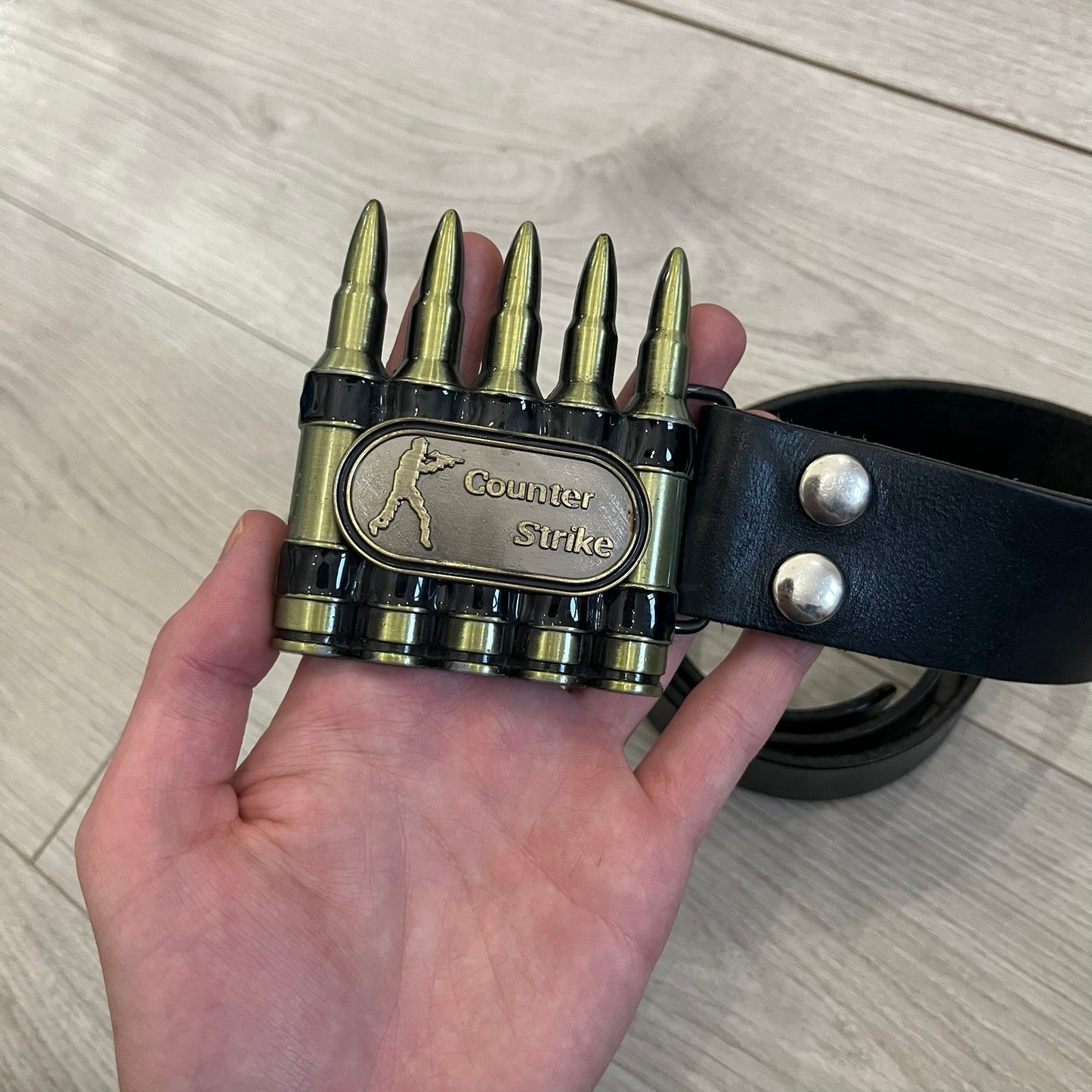 Counter Strike Metal Belt Buckle featuring five metal bullets with black vitreous enamel stripes. Includes a metal dog tag plaque on the front with “Counter Strike” text and the iconic Counter Strike logo of a shooter.
