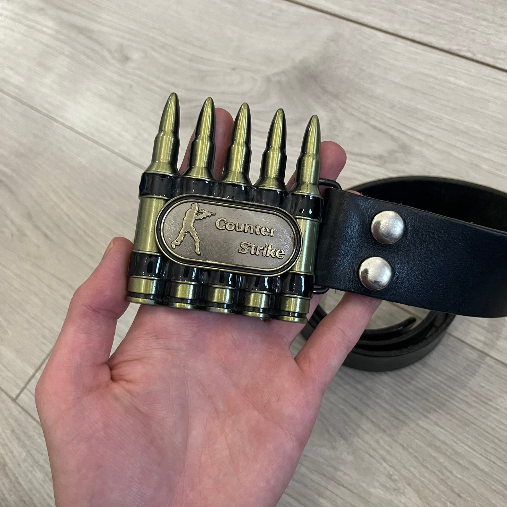 Counter Strike Metal Belt Buckle featuring five metal bullets with black vitreous enamel stripes. Includes a metal dog tag plaque on the front with “Counter Strike” text and the iconic Counter Strike logo of a shooter.