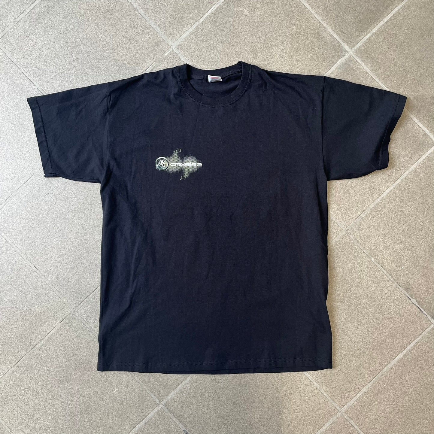 Crysis 2 Promo 2011 Black Tee features a black design with a small Crysis 2 logo on the front right chest printed over a mesh-style graphic inspired by the game. The back features a large graphic of a Force Recon Marine holding a weapon, combined with additional futuristic mesh details from the Crysis universe. Made on a Fruit of the Loom blank.
