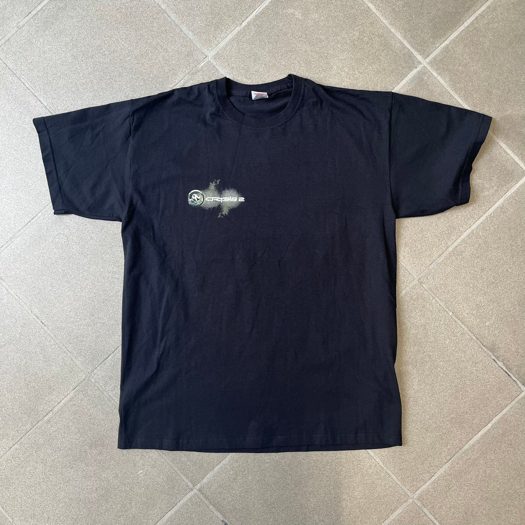 Crysis 2 Promo 2011 Black Tee features a black design with a small Crysis 2 logo on the front right chest printed over a mesh-style graphic inspired by the game. The back features a large graphic of a Force Recon Marine holding a weapon, combined with additional futuristic mesh details from the Crysis universe. Made on a Fruit of the Loom blank.
