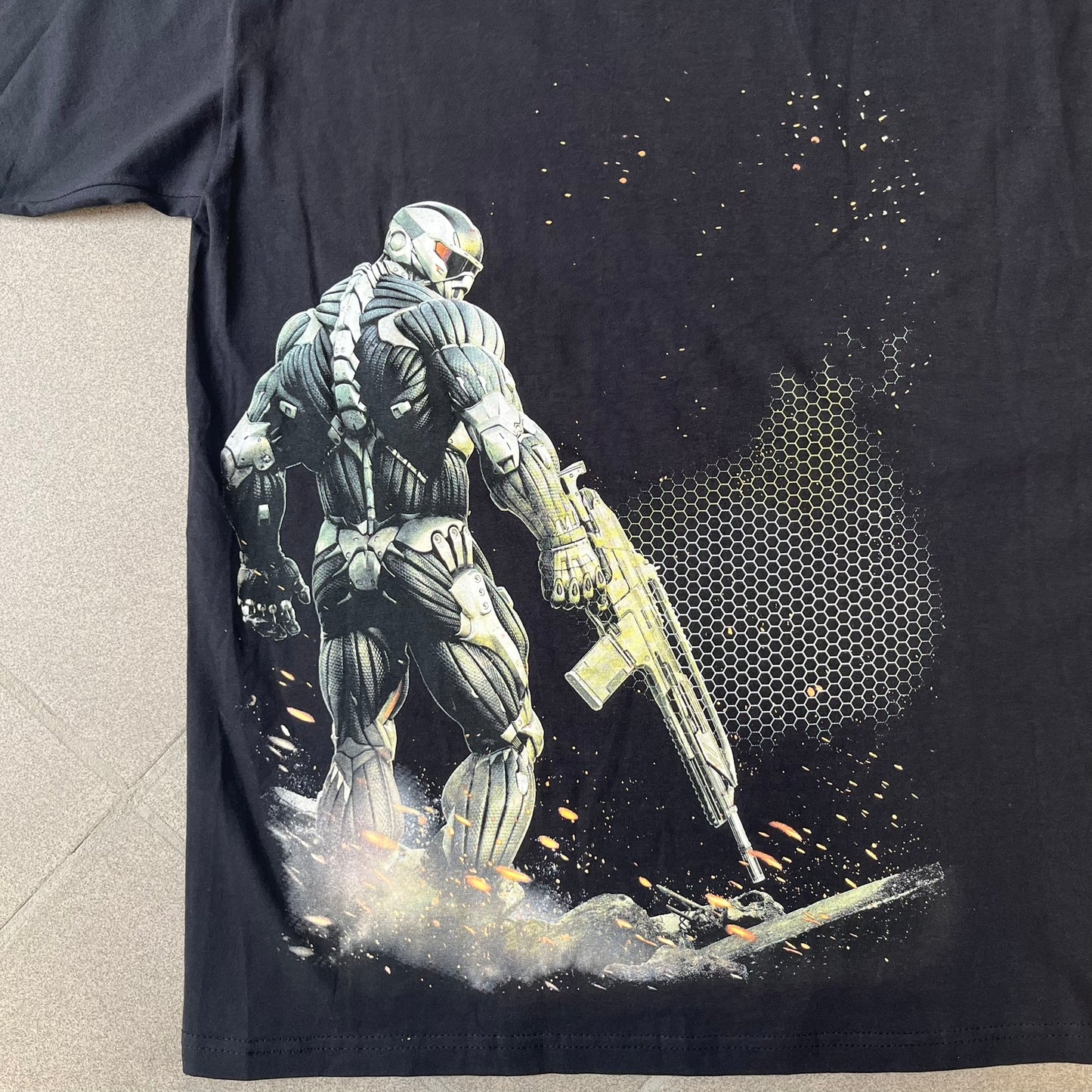 Crysis 2 Promo 2011 Black Tee features a black design with a small Crysis 2 logo on the front right chest printed over a mesh-style graphic inspired by the game. The back features a large graphic of a Force Recon Marine holding a weapon, combined with additional futuristic mesh details from the Crysis universe. Made on a Fruit of the Loom blank.
