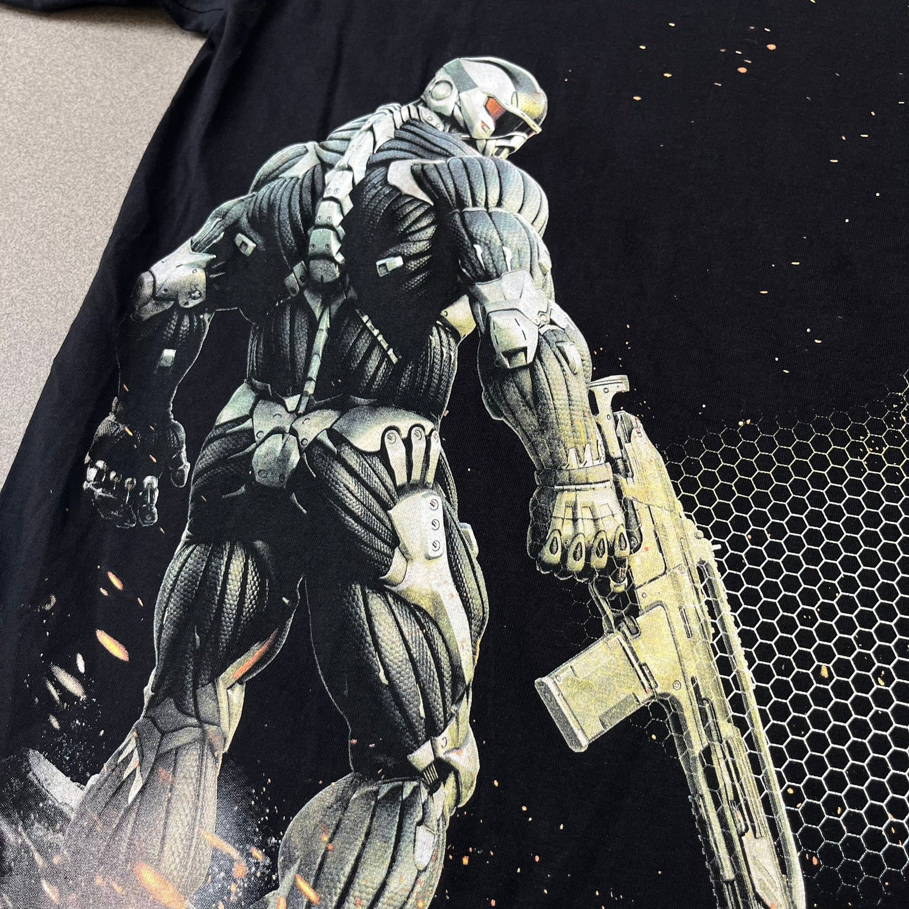 Crysis 2 Promo 2011 Black Tee features a black design with a small Crysis 2 logo on the front right chest printed over a mesh-style graphic inspired by the game. The back features a large graphic of a Force Recon Marine holding a weapon, combined with additional futuristic mesh details from the Crysis universe. Made on a Fruit of the Loom blank.
