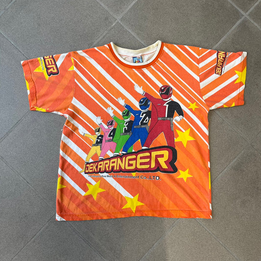 Dekaranger 2004 Orange All Over Print Tee is an orange all-over print T-shirt featuring the same design on both front and back, showing five Dekarangers lined up with "Dekaranger" text and licensing below, set against a background of white stripes and yellow stars. Dekaranger branding appears on both sleeves, and it carries a Gaoranger neck tag.
