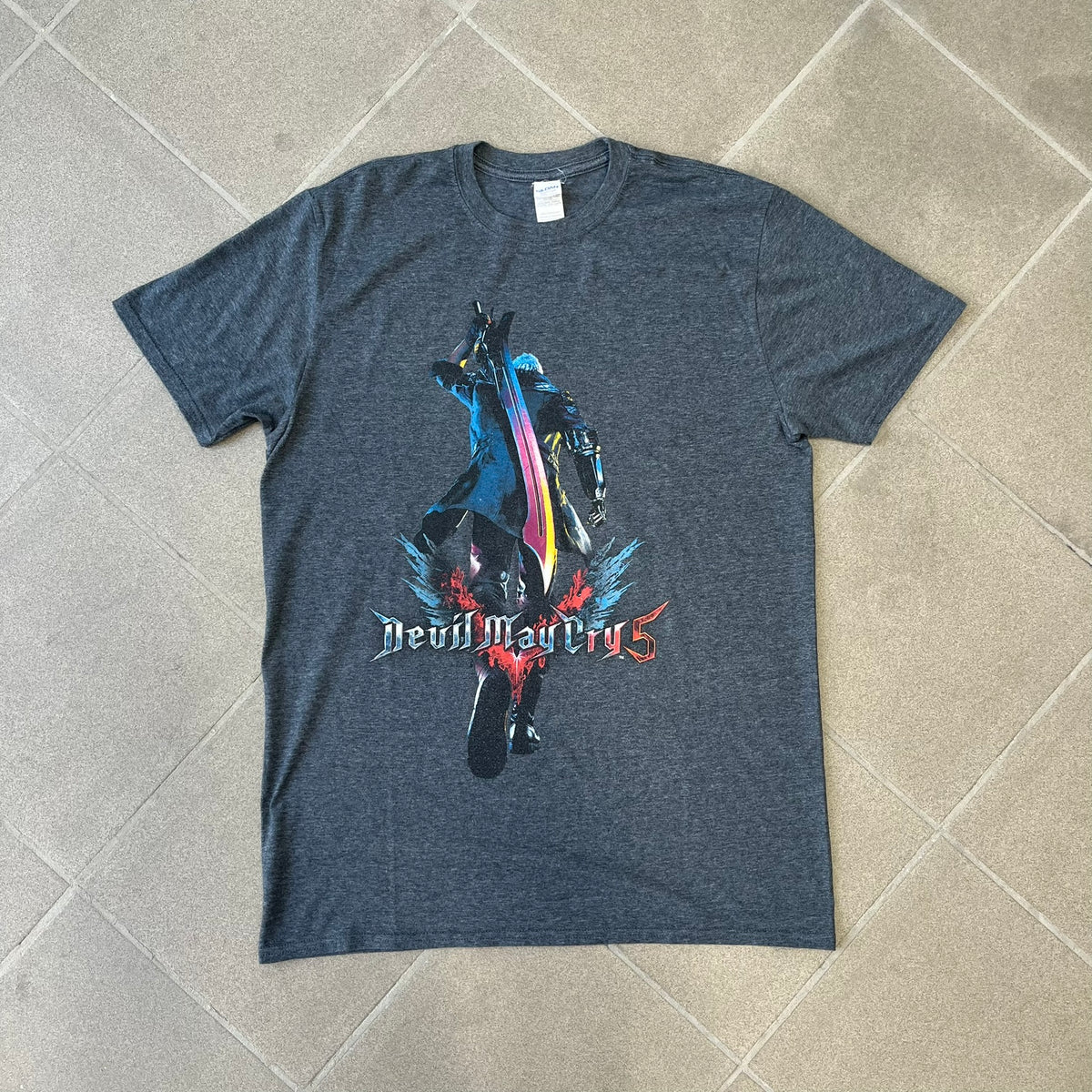Devil May Cry 5 Promo 2019 Gray Tee is made on a Gildan blank in grey cotton. The front features the Devil May Cry 5 game cover but only with Nero holding his sword, along with large “Devil May Cry 5” text. Made as a promotional T-shirt for the game.