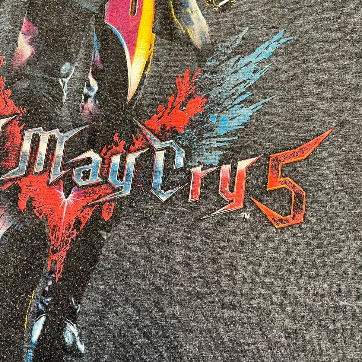 Devil May Cry 5 Promo 2019 Gray Tee is made on a Gildan blank in grey cotton. The front features the Devil May Cry 5 game cover but only with Nero holding his sword, along with large “Devil May Cry 5” text. Made as a promotional T-shirt for the game.