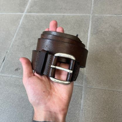 Diesel 2000's Brown Leather Belt features a brown 100% cow leather construction with a simple silver-tone buckle. A small leather piece with Diesel text is attached to the buckle and rotates freely. The belt is marked “Extra Tough,” with gold Diesel text printed on the inside. Made in Italy, with an additional attached section at the end for adjusting the length.
