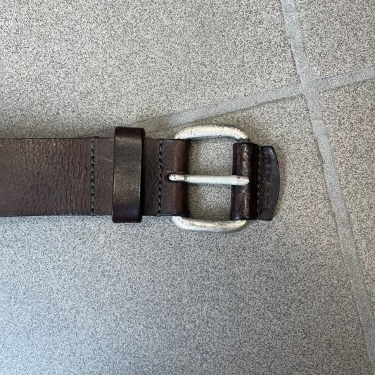 Diesel 2000's Brown Leather Belt features a brown 100% cow leather construction with a simple silver-tone buckle. A small leather piece with Diesel text is attached to the buckle and rotates freely. The belt is marked “Extra Tough,” with gold Diesel text printed on the inside. Made in Italy, with an additional attached section at the end for adjusting the length.
