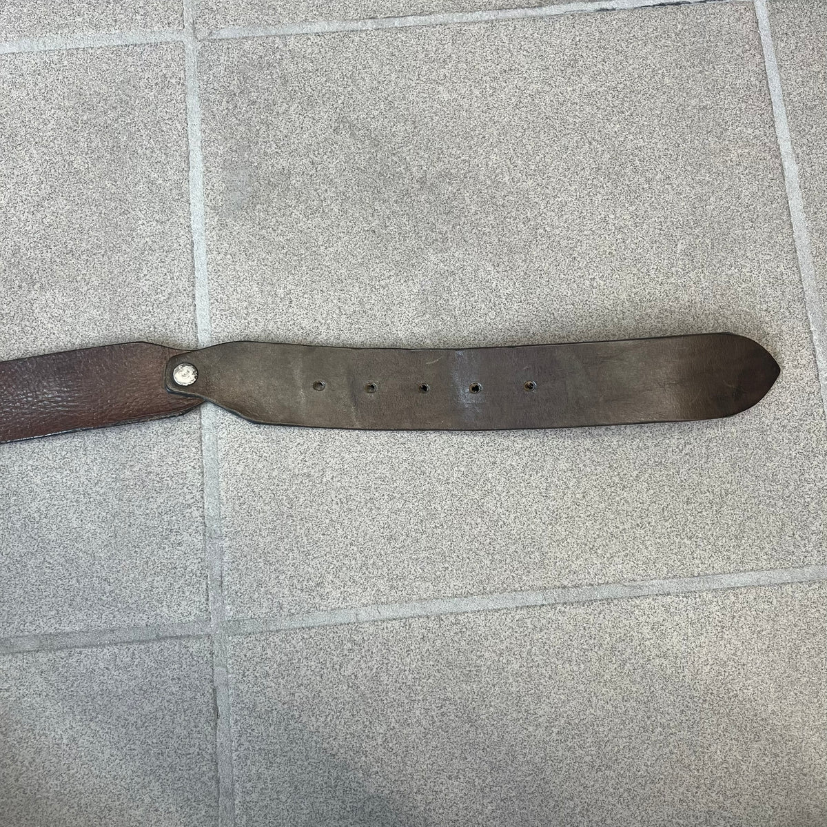 Diesel 2000's Brown Leather Belt features a brown 100% cow leather construction with a simple silver-tone buckle. A small leather piece with Diesel text is attached to the buckle and rotates freely. The belt is marked “Extra Tough,” with gold Diesel text printed on the inside. Made in Italy, with an additional attached section at the end for adjusting the length.
