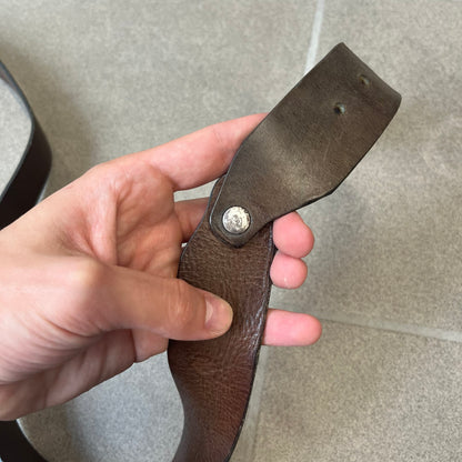 Diesel 2000's Brown Leather Belt features a brown 100% cow leather construction with a simple silver-tone buckle. A small leather piece with Diesel text is attached to the buckle and rotates freely. The belt is marked “Extra Tough,” with gold Diesel text printed on the inside. Made in Italy, with an additional attached section at the end for adjusting the length.
