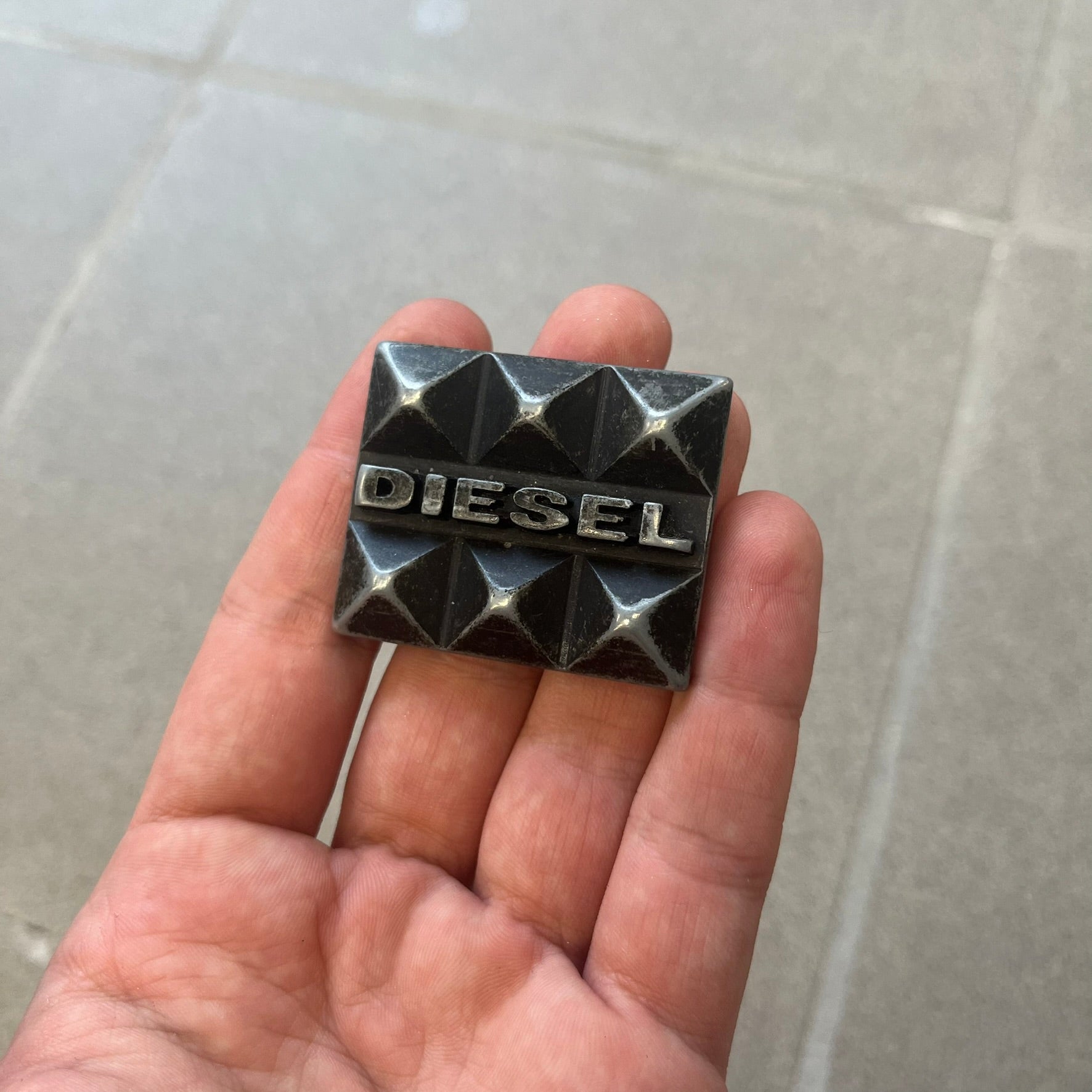 Diesel 2000s Changeable Buckles Set includes a Diesel belt buckle system with interchangeable front pieces. The base buckle features two snap buttons that allow different designs to be attached. The set includes three interchangeable buckles: a Diesel logo design with studs, a circular buckle with the Mohawk character logo, and a bronze pyramid logo design. Comes with the original dust bag.
