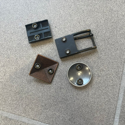 Diesel 2000s Changeable Buckles Set includes a Diesel belt buckle system with interchangeable front pieces. The base buckle features two snap buttons that allow different designs to be attached. The set includes three interchangeable buckles: a Diesel logo design with studs, a circular buckle with the Mohawk character logo, and a bronze pyramid logo design. Comes with the original dust bag.
