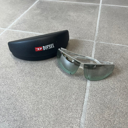 Diesel 2000's Clear Jumbo Sunglasses feature thin silver-tone wire temples with clear plastic sections extending over the ends and front of the frame. The lenses have a grey-tinted transparent finish, with visible screws on the front. A small silver Diesel logo is placed on the side, with white Diesel text printed in the corner of one lens.
