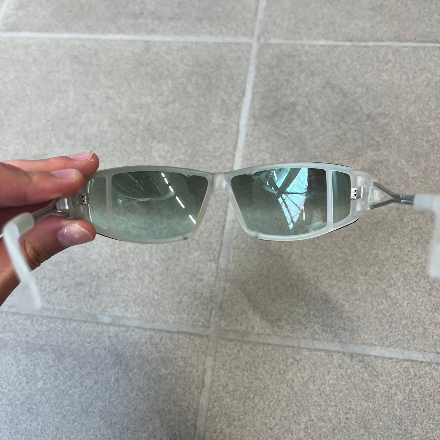 Diesel 2000's Clear Jumbo Sunglasses feature thin silver-tone wire temples with clear plastic sections extending over the ends and front of the frame. The lenses have a grey-tinted transparent finish, with visible screws on the front. A small silver Diesel logo is placed on the side, with white Diesel text printed in the corner of one lens.

