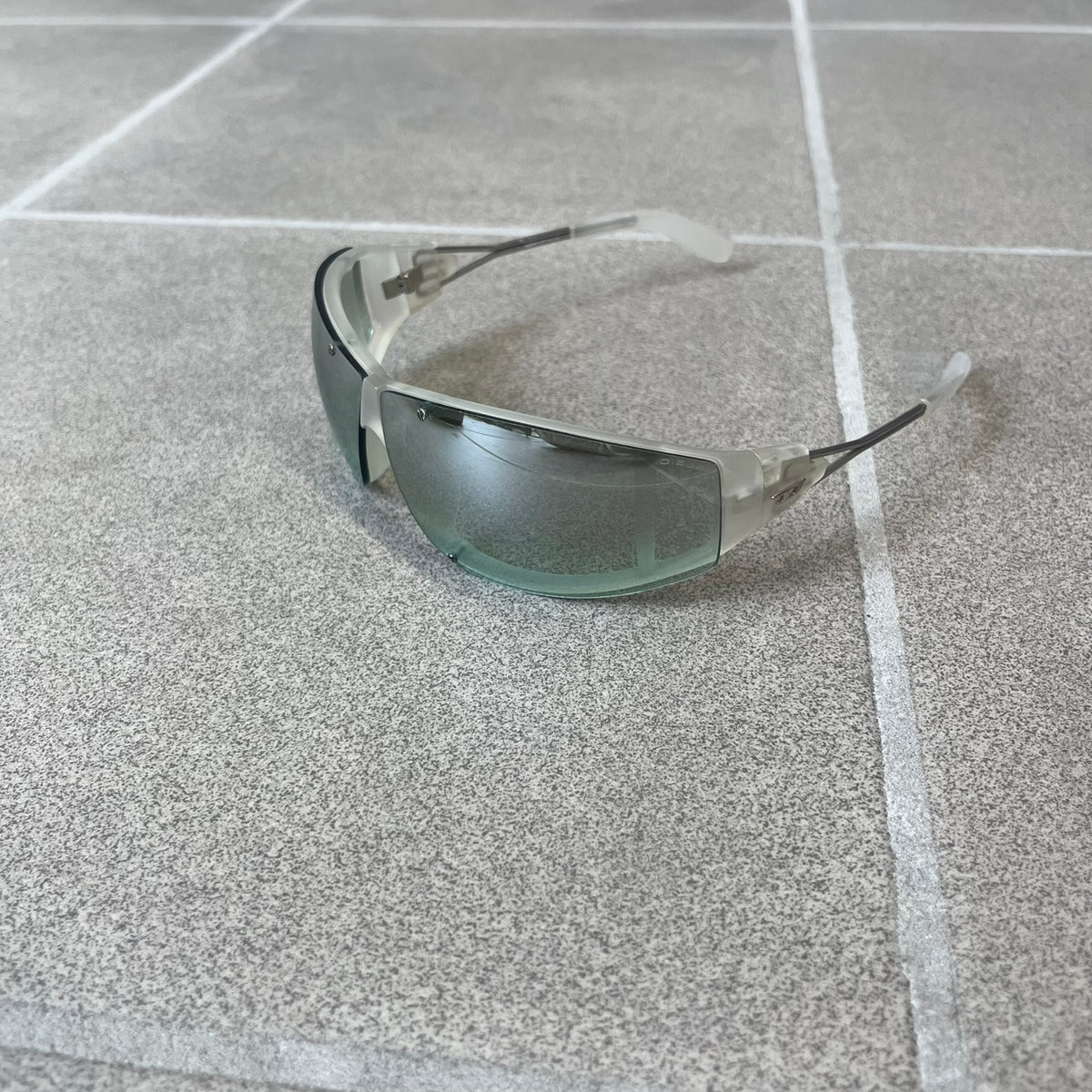 Diesel 2000's Clear Jumbo Sunglasses feature thin silver-tone wire temples with clear plastic sections extending over the ends and front of the frame. The lenses have a grey-tinted transparent finish, with visible screws on the front. A small silver Diesel logo is placed on the side, with white Diesel text printed in the corner of one lens.

