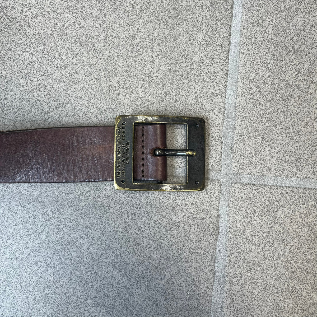 Diesel 2000's Only The Brave Brown Leather Belt features a brown 100% cow leather construction with a bronze-tone buckle. The buckle has engraved Diesel branding, including “Only The Brave Since 1978” text and other details. The belt is marked “Extra Tough,” with gold Diesel text printed on the inside. Made in Italy.
