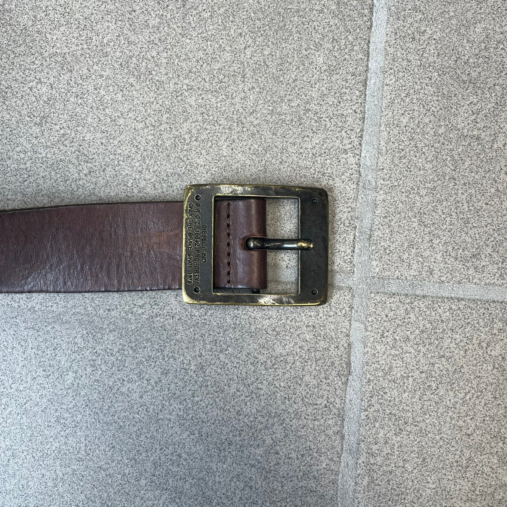 Diesel 2000's Only The Brave Brown Leather Belt features a brown 100% cow leather construction with a bronze-tone buckle. The buckle has engraved Diesel branding, including “Only The Brave Since 1978” text and other details. The belt is marked “Extra Tough,” with gold Diesel text printed on the inside. Made in Italy.

