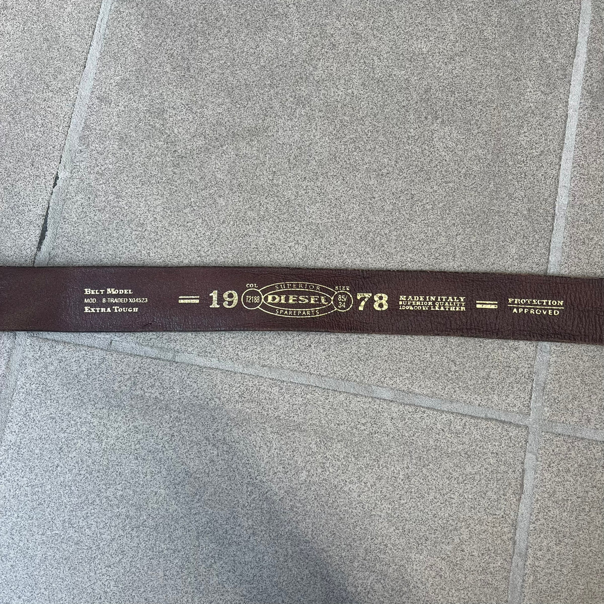 Diesel 2000's Only The Brave Brown Leather Belt features a brown 100% cow leather construction with a bronze-tone buckle. The buckle has engraved Diesel branding, including “Only The Brave Since 1978” text and other details. The belt is marked “Extra Tough,” with gold Diesel text printed on the inside. Made in Italy.
