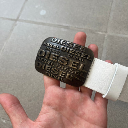 Diesel 2000s Repeat Logo White Leather Belt features a white leather strap with a rectangular bronze-tone buckle. The buckle is decorated with a repeating Diesel text logo pattern in different sizes, creating a layered branded design. Made in Italy.
