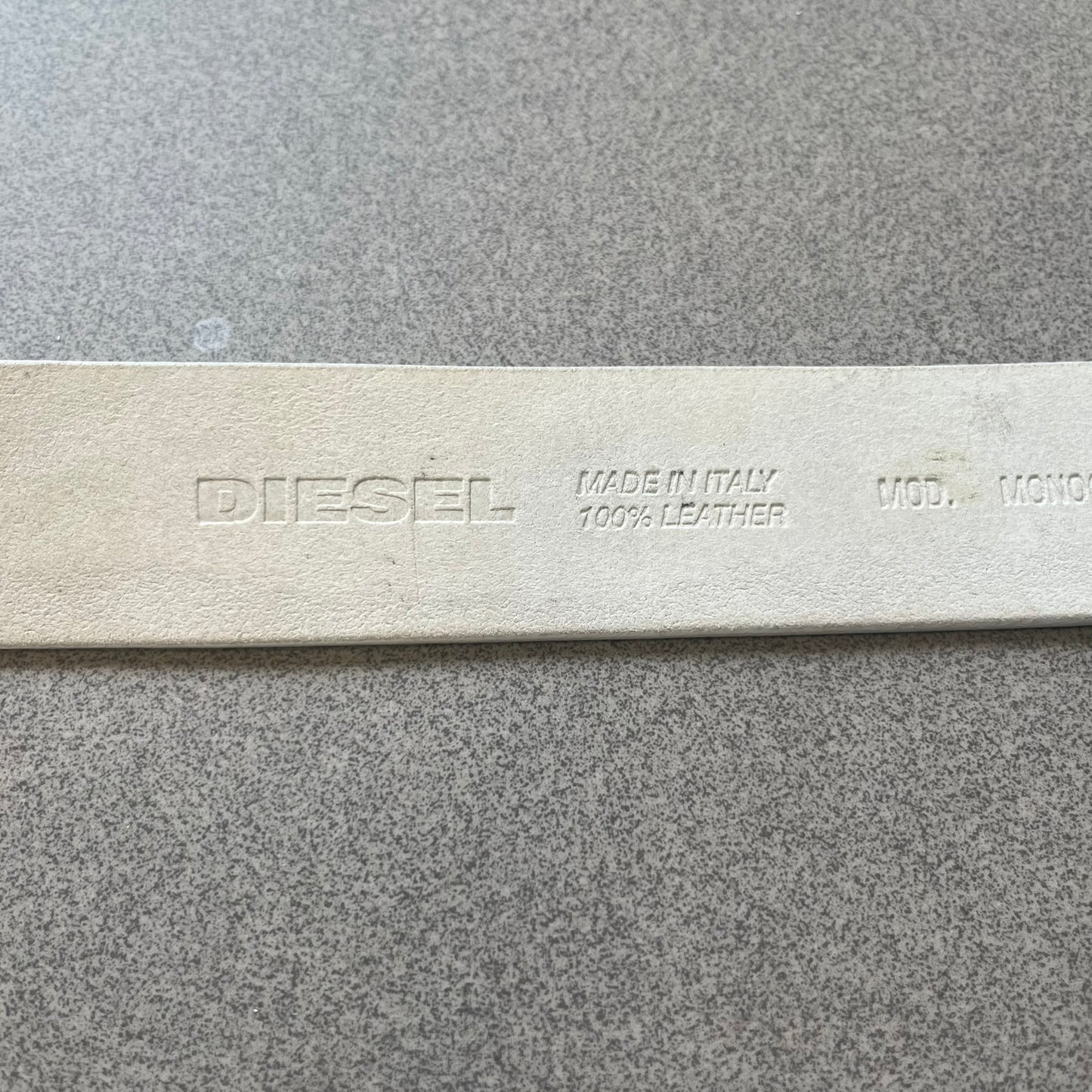 Diesel 2000s Repeat Logo White Leather Belt features a white leather strap with a rectangular bronze-tone buckle. The buckle is decorated with a repeating Diesel text logo pattern in different sizes, creating a layered branded design. Made in Italy.
