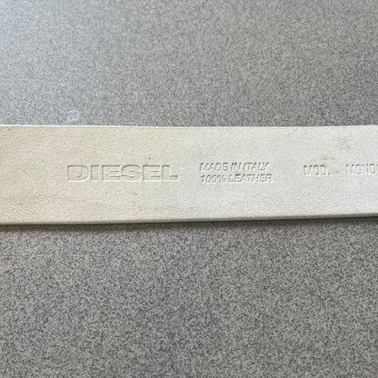 Diesel 2000s Repeat Logo White Leather Belt features a white leather strap with a rectangular bronze-tone buckle. The buckle is decorated with a repeating Diesel text logo pattern in different sizes, creating a layered branded design. Made in Italy.
