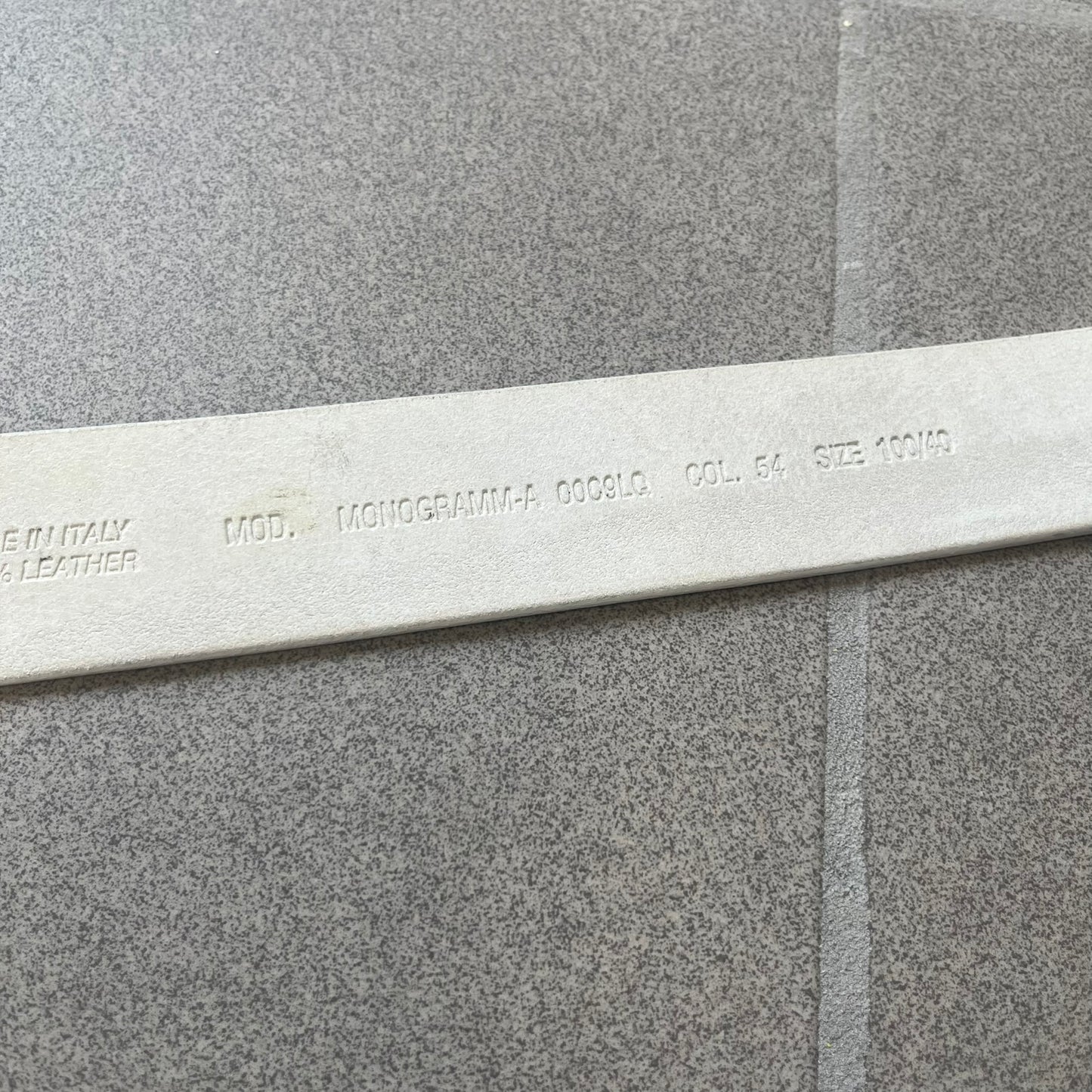 Diesel 2000s Repeat Logo White Leather Belt features a white leather strap with a rectangular bronze-tone buckle. The buckle is decorated with a repeating Diesel text logo pattern in different sizes, creating a layered branded design. Made in Italy.

