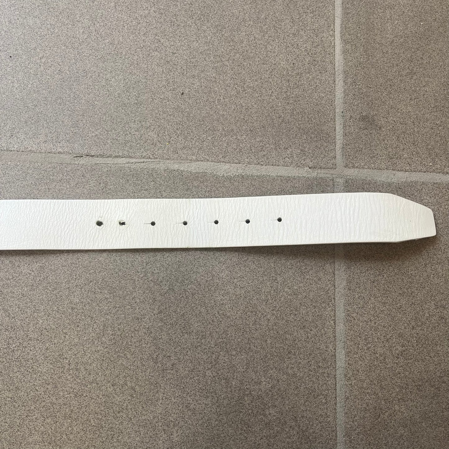 Diesel 2000s Repeat Logo White Leather Belt features a white leather strap with a rectangular bronze-tone buckle. The buckle is decorated with a repeating Diesel text logo pattern in different sizes, creating a layered branded design. Made in Italy.
