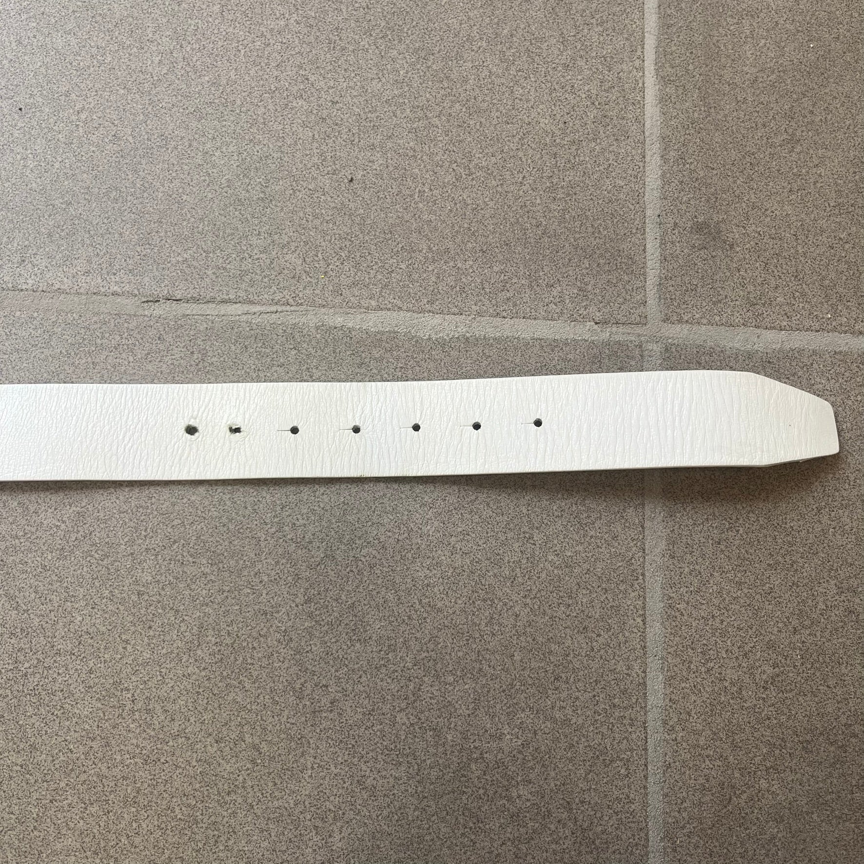 Diesel 2000s Repeat Logo White Leather Belt features a white leather strap with a rectangular bronze-tone buckle. The buckle is decorated with a repeating Diesel text logo pattern in different sizes, creating a layered branded design. Made in Italy.
