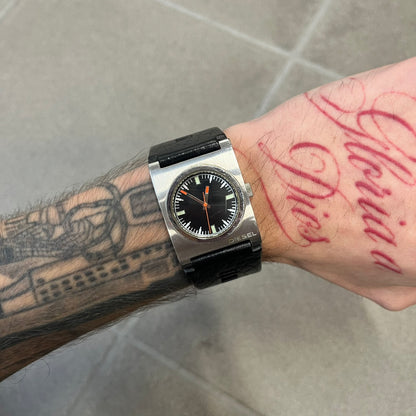 Diesel 2000’s Square DZ2107 Analog Watch has a square stainless steel case with an engraved Diesel logo in the bottom right corner. The circular black dial has orange hands, and the watch is fitted with a black leather strap.