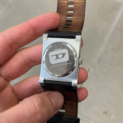 Diesel 2000’s Square DZ2107 Analog Watch has a square stainless steel case with an engraved Diesel logo in the bottom right corner. The circular black dial has orange hands, and the watch is fitted with a black leather strap.