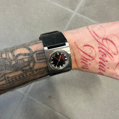 Diesel 2000’s Square DZ2107 Analog Watch has a square stainless steel case with an engraved Diesel logo in the bottom right corner. The circular black dial has orange hands, and the watch is fitted with a black leather strap.