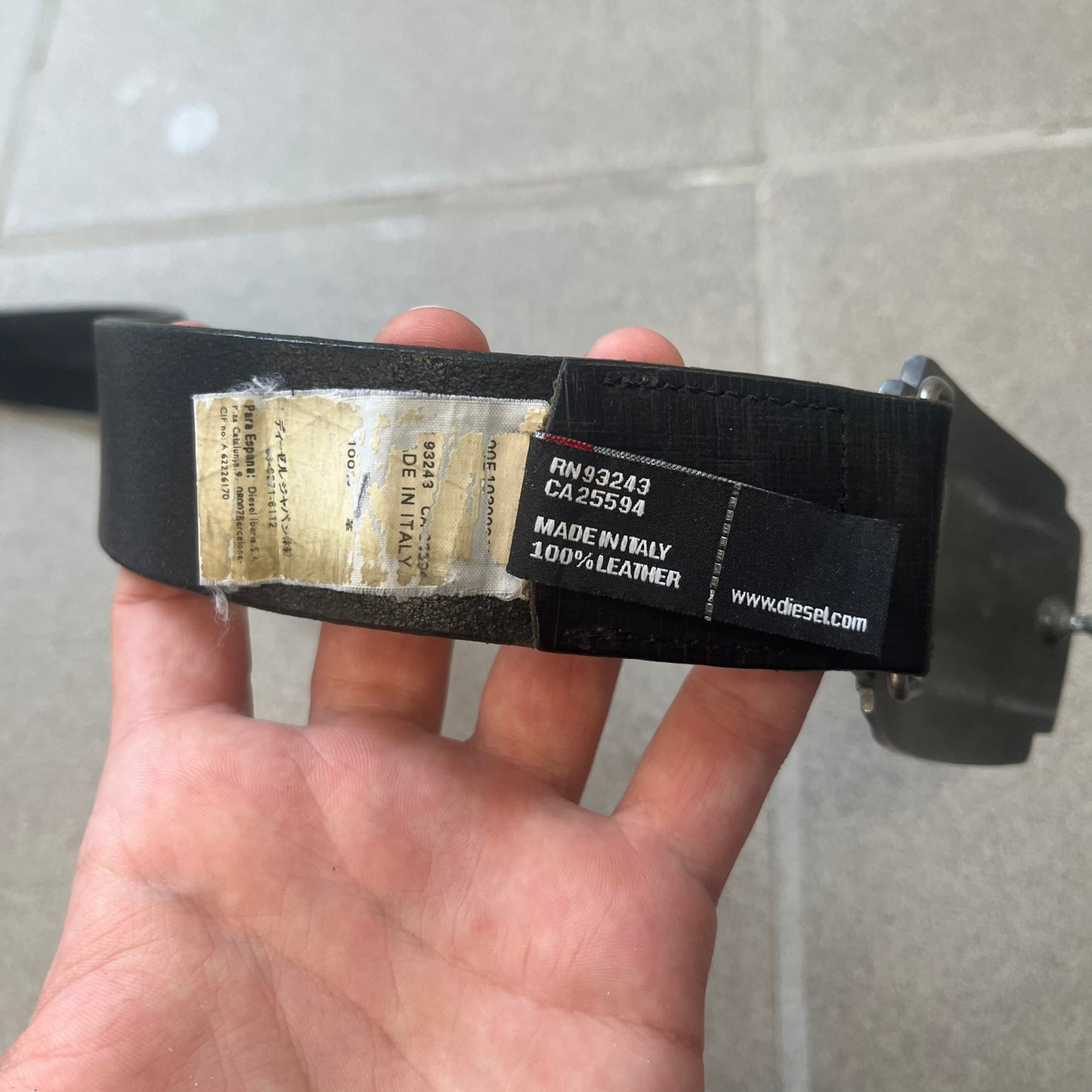 Diesel 2000s Vintage Buckle Leather Belt features a black leather strap made in Italy. The belt has a large rectangular metal buckle designed to look like a worn metal sheet, with a Diesel logo formed from small perforated holes. The buckle includes visible screws on the sides and the belt is made from 100% leather.
