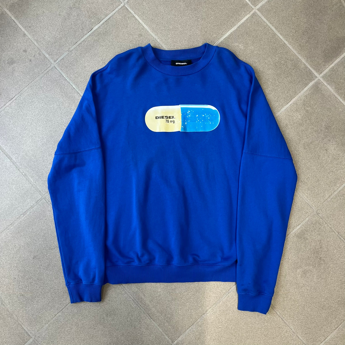 Diesel 2017 "78 mg Pill" Blue Crewneck is a blue, 100% cotton crewneck featuring a large pill graphic in yellow and blue, with black "DIESEL 78 mg" text printed on the yellow half.